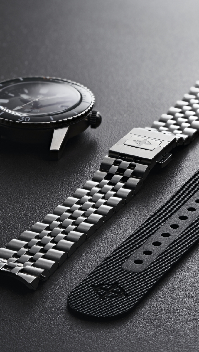A 5-link bracelet shown next to a watch case and a rubber strap A 5-link bracelet shown next to a watch case and a rubber strap