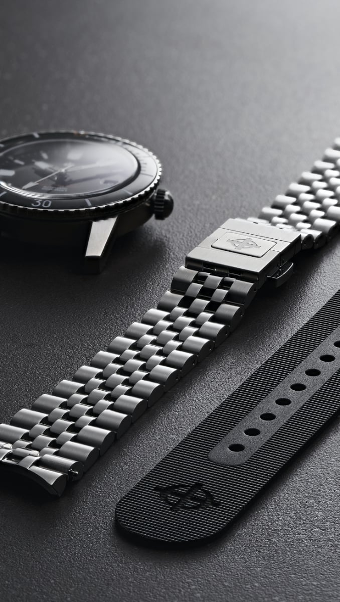 A 5-link bracelet shown next to a watch case and a rubber strap A 5-link bracelet shown next to a watch case and a rubber strap